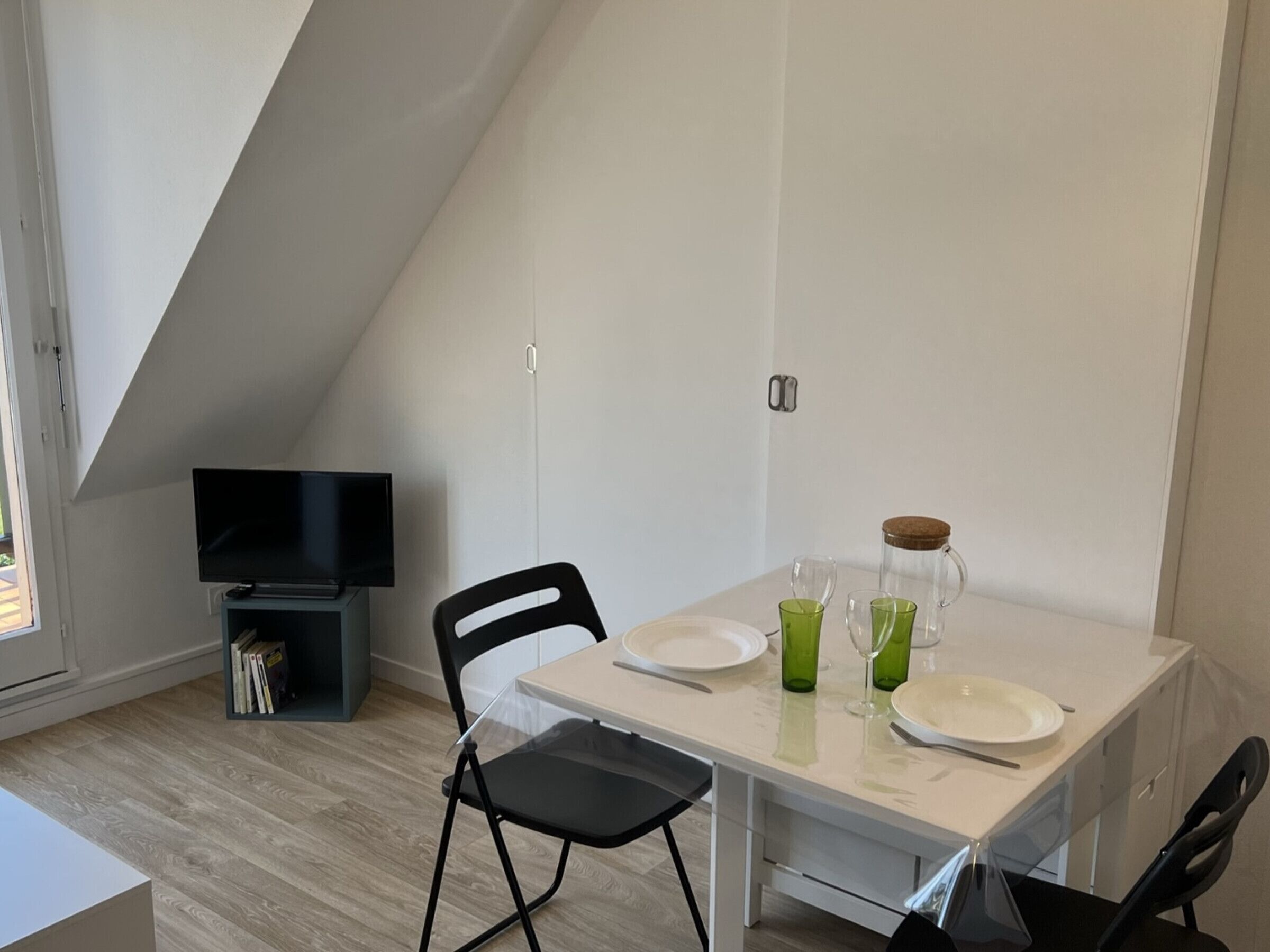 A small dining area with a table, chairs, a television, and a bookshelf.