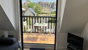Ein Balkon mit Tisch und Stühlen, einem Fernseher und Blick auf Häuser in der Ferne.