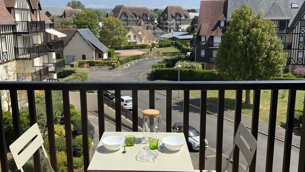 Ein Balkon mit Tisch für Zwei, mit Blick auf eine Wohnstraße mit Häusern und Grünflächen.