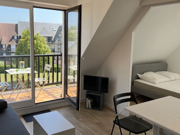 A modern loft bedroom with a large sliding glass door leading to a balcony, a TV, a bed, and a small table.