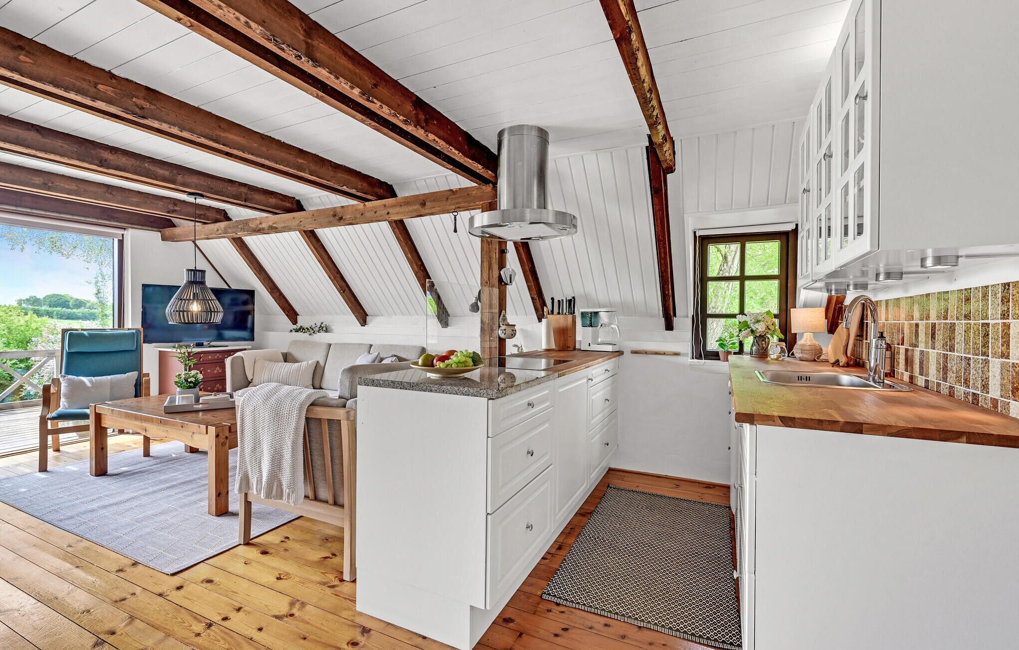 Una cocina moderna con armarios blancos, techo de madera y un ventanal con vistas a zonas verdes.