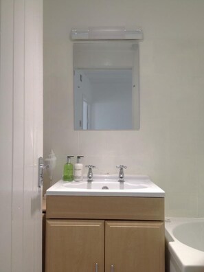 A bathroom with a white sink, two faucets, a mirror above the sink, and a bathtub to the right.