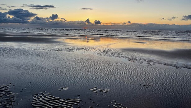 A beach scene with calm waves and a sunset.