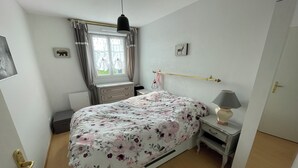 A bedroom with a bed, bedside table, lamp, window with curtains, and a wall-mounted picture.