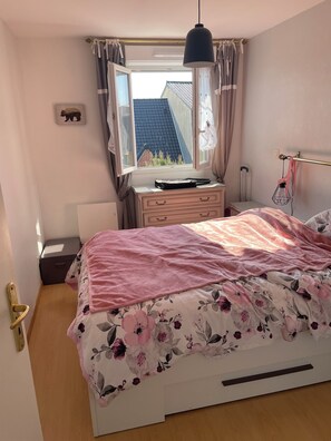 A bedroom with a bed, a dresser, a window with curtains, and a radiator.