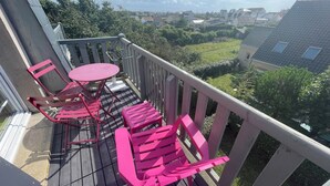 A balcony with a table and chairs, overlooking a residential area with houses and greenery.