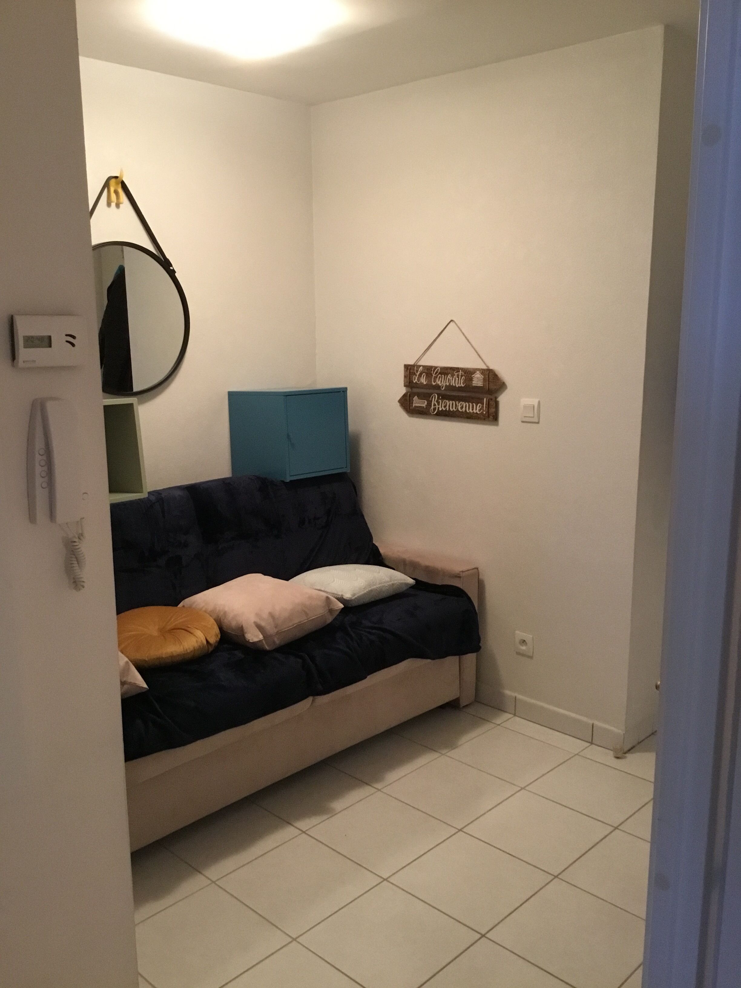 A room with a blue sofa, a small table, a wall-mounted mirror, and a welcome sign.