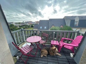 A balcony with a table and chairs, a dog lying on the floor, and a view of houses in the background.
