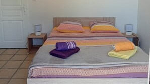 Een net opgemaakt bed met beddengoed met een patroon, een ingelijst foto aan de muur en bedlampjes.