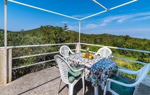 A balcony with a table set for two, surrounded by white chairs with green cushions, overlooking a lush green landscape. - 2 bedroom nice home in Molat (Molat)