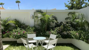 A small patio area with a round table and four chairs, surrounded by lush greenery and flowering plants. - Palm Beach Stunning Villa 13-beds 10-baths -26ppl (Noord)