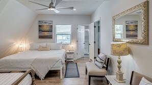 Ein Schlafzimmer mit Bett, Nachttischen, einem Schreibtisch, einem Stuhl, einer Lampe, einem Deckenventilator und Bildern an den Wänden.