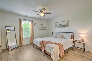 Ein Schlafzimmer mit Bett, Nachttisch, Fenster mit Vorhängen und einem Bild an der Wand.