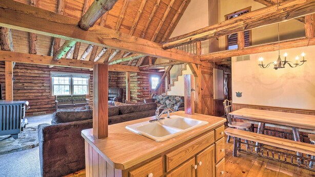 A rustic cabin interior with a wooden dining table, a kitchen area with a sink, and a cozy seating area with a fireplace. - Rustic Zanesville Getaway w/ Expansive Yard! (Zanesville)