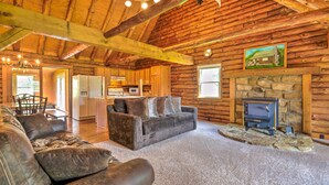 A log cabin interior with a fireplace, a sofa, a dining area, and a kitchen. - Rustic Zanesville Getaway w/ Expansive Yard! (Zanesville)