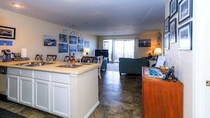 Una cocina con una isla grande, un comedor con sillas, un sofá y un televisor al fondo.