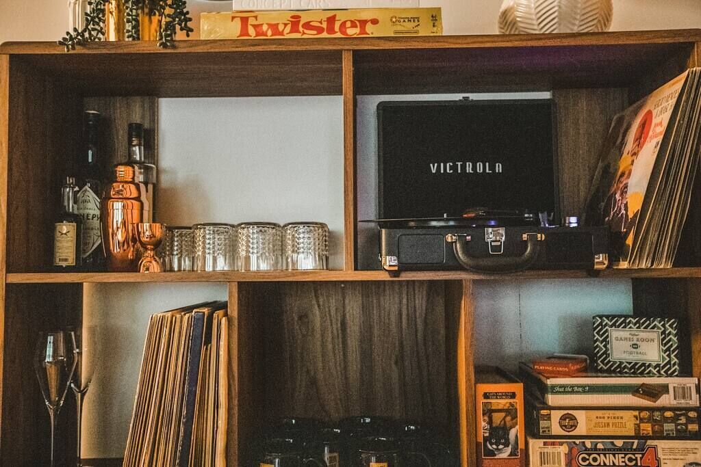 A wooden shelf with various items including a box labeled 'Twister', a 'VICTOROLA' case, and several board games.