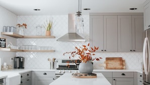 Een moderne keuken met witte kasten, een centraal eiland, roestvrijstalen apparatuur en hangende吊灯.