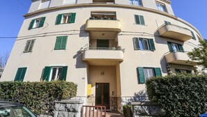 Un immeuble à plusieurs étages, doté de balcons, d’une entrée centrale et d’une base en pierre.