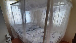 Une chambre avec un lit recouvert d’une moustiquaire, une couvre-lit à motifs floraux et un mur uni avec un interrupteur.