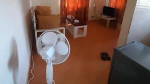 Une petite chambre comprenant un lit, une petite table, une télévision et un ventilateur.