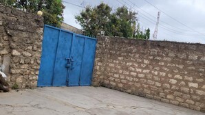 Une cour avec une porte bleue, des murs en pierre et un sol en béton.