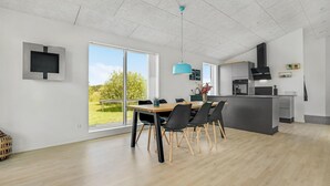 A modern kitchen with a large island, a dining area with a wooden table and chairs, and a view of greenery outside. - 3 bedroom beautiful home in Jerup (Jerup)