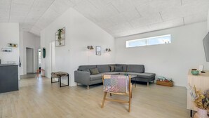 A spacious living area with a grey sofa, a small table with a patterned tablecloth, and a wooden floor. - 3 bedroom beautiful home in Jerup (Jerup)