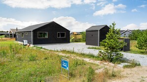 A modern building with a black exterior, a gravel driveway, and a playground in the background. - 3 bedroom beautiful home in Jerup (Jerup)