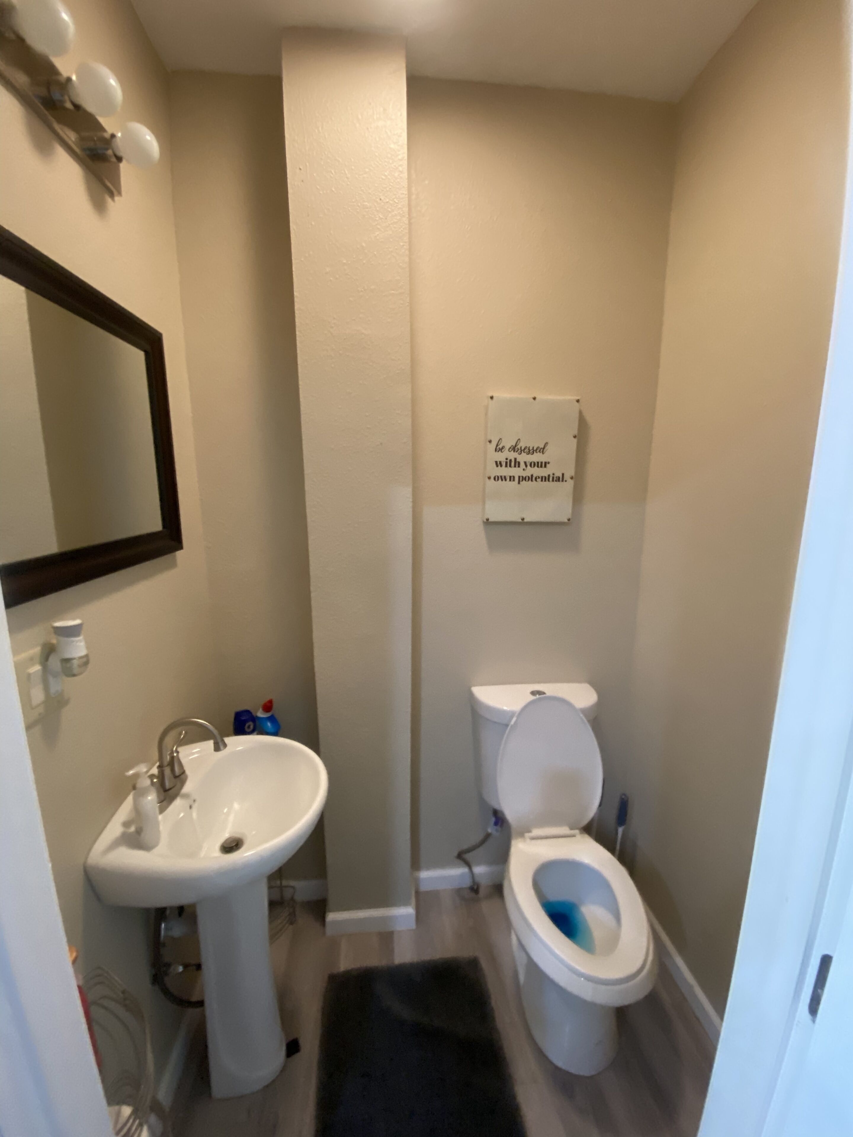 A bathroom with a sink, mirror, toilet, and a motivational sign on the wall.