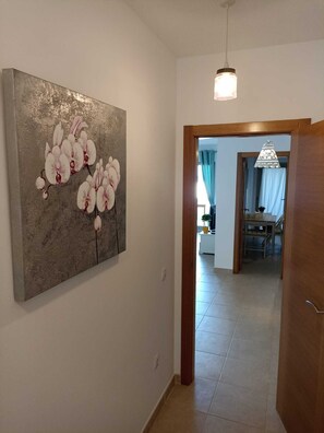 A hallway with a large abstract painting on the left, a wooden door frame on the right, and a view into a room with a chandelier.