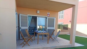 Une terrasse extérieure avec une table et des chaises, une porte-fenêtre coulissante et un petit jardin.