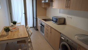Une cuisine compacte équipée d’un four à micro-ondes, d’un four et d’un lave-linge. On y trouve une table à manger avec des chaises et une petite plante.