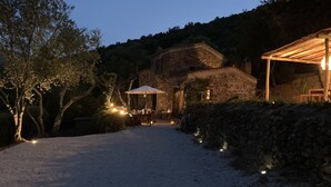 A gravel path leading to a stone building with a covered outdoor seating area, surrounded by trees and stone walls.