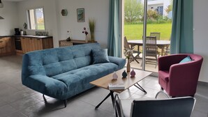 A modern living room with a blue sofa, a wooden coffee table, and a red armchair. There is a sliding glass door leading to a patio with outdoor furniture. - House 3***6 persons sea view in Paimpol (Paimpol)