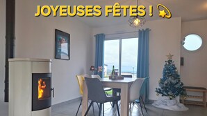 A cozy living room with a wood-burning stove, a dining table with chairs, a Christmas tree, and a large window offering a view. - House 3***6 persons sea view in Paimpol (Paimpol)