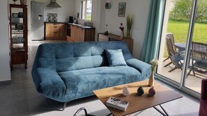 A modern living room with a blue sofa, a wooden coffee table, and a view of the outdoor patio. - House 3***6 persons sea view in Paimpol (Paimpol)