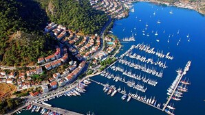 An aerial view of a coastal town with a marina filled with boats, surrounded by residential buildings and greenery. - Mykonut Erna Apart Hotel (Fethiye)