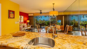 A modern kitchen with a granite countertop, stainless steel sink, and a dining area with a view of the outdoors.