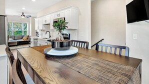 Une cuisine moderne avec des meubles blancs, une table à manger agrémentée d’un set de table en fibres tressées et une plante en pot qui sert de centre de table.