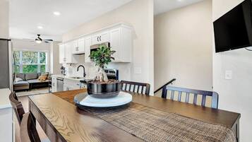 Una cocina moderna con armarios blancos, una mesa de comedor con un mantel tejido y un centro de mesa con planta en maceta.