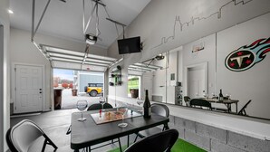 Un espace intérieur moderne comprenant une table à manger, des chaises, un téléviseur fixé au mur et une porte de garage donnant sur l’extérieur.