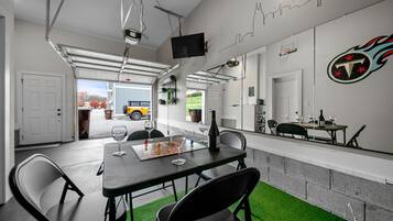 A modern indoor space with a dining table, chairs, a TV mounted on the wall, and a garage door leading outside.