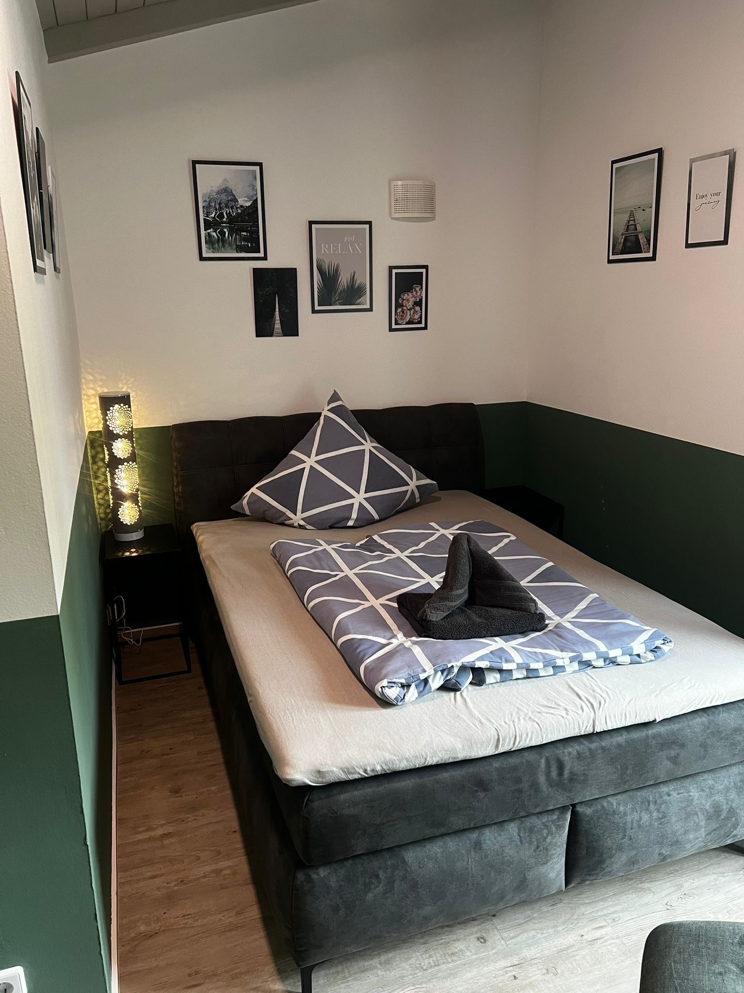 Une chambre à coucher bien rangée, avec un lit, des oreillers et une table de chevet sur laquelle se trouve une lampe.