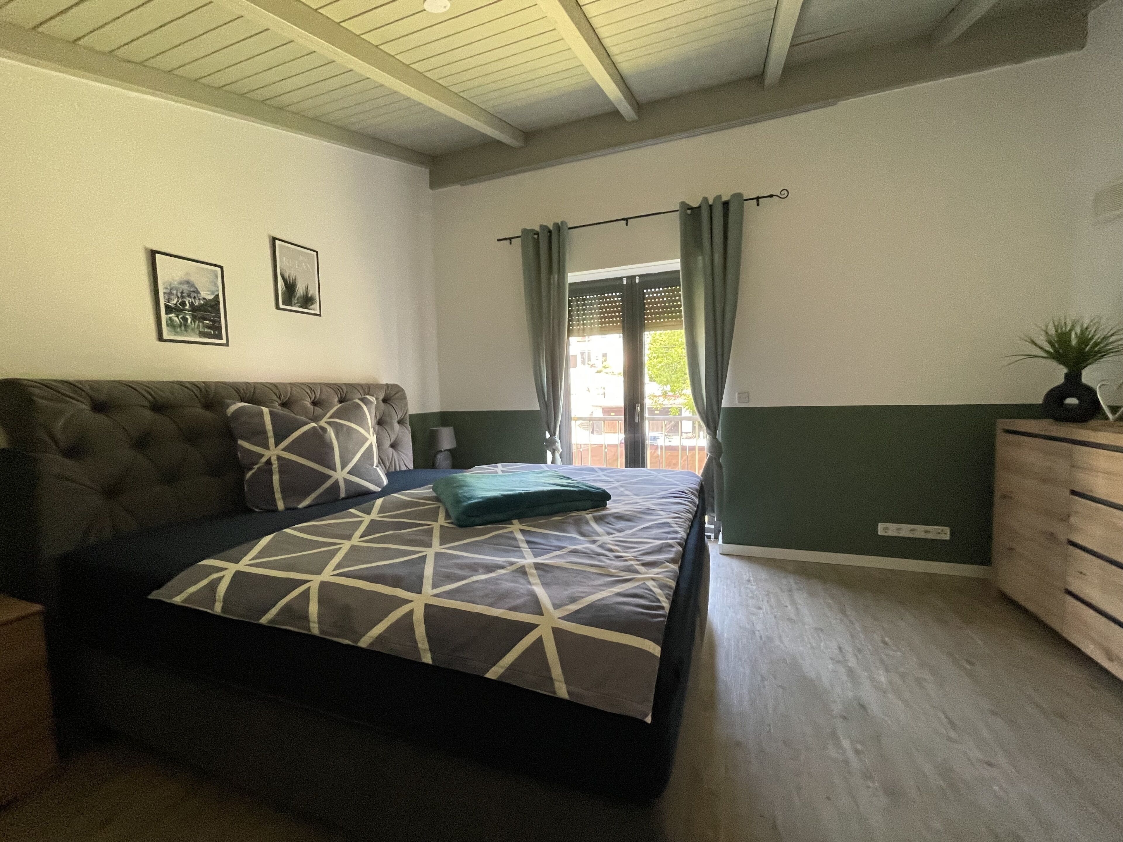 Une chambre avec un grand lit, une commode et un balcon avec des rideaux.