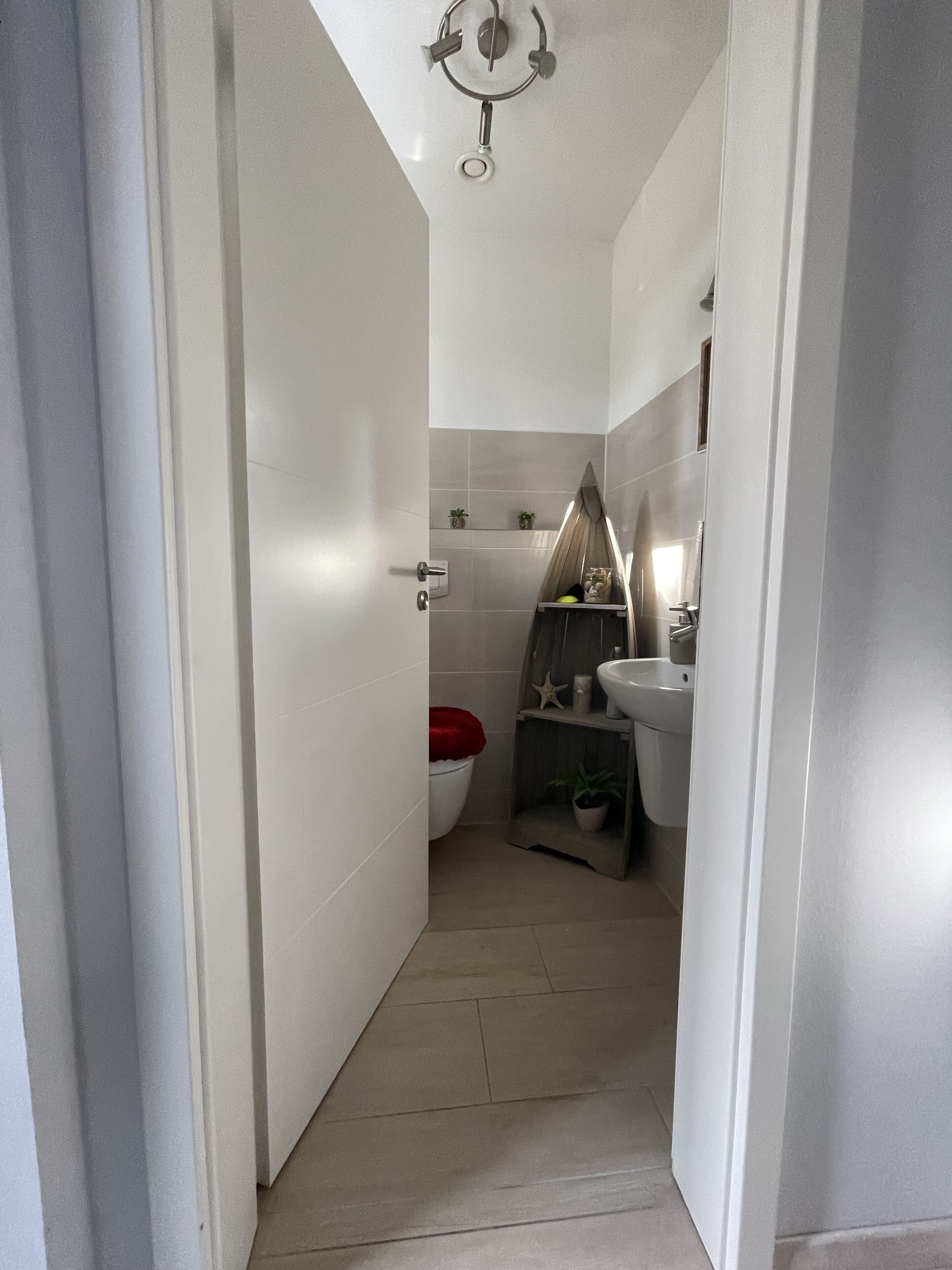 En smal gang, der fører til et badeværelse med toilet, pissoir og håndvask.