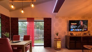 Een moderne woonkamer met een houten eettafel, rode stoelen, een aan de muur bevestigde televisie en een klein houten kastje.