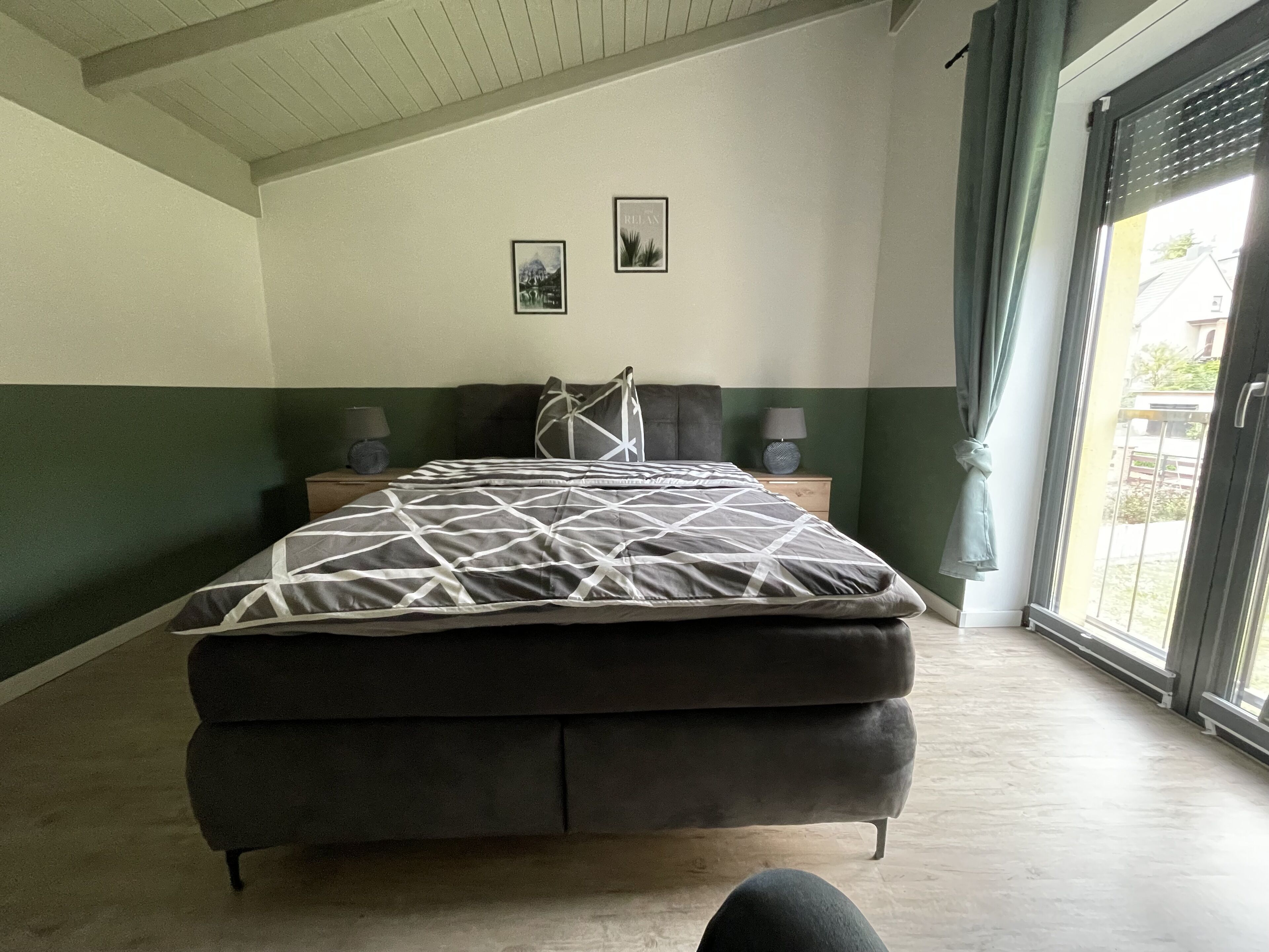 Ein Schlafzimmer mit einem Bett, zwei Nachttischen, einem Fenster mit Vorhängen und einer Wand mit zwei gerahmten Bildern.