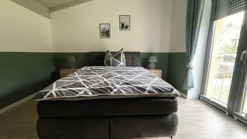 Ein Schlafzimmer mit einem Bett, zwei Nachttischen, einem Fenster mit Vorhängen und einer Wand mit zwei gerahmten Bildern.