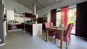 Een moderne keuken met een centraal eiland, een eetgedeelte met rode stoelen en een groot raam met rode gordijnen.